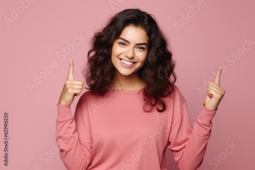 Beautiful fictional brunette model portrait pointing up with her fingers. Isolated on a plain colored background. Generative AI.