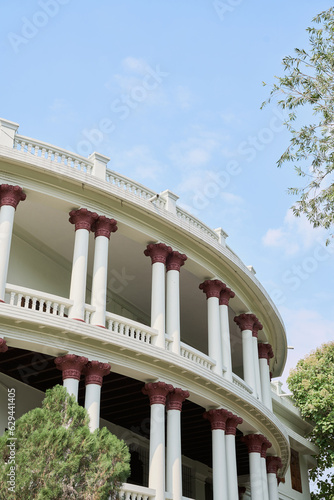 Photo A white building with pillars, maroon accent and blue cloudy sky
