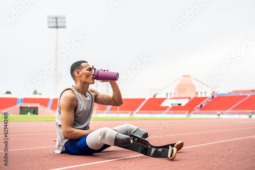 Fototapeta Naklejka Na Ścianę i Meble -  Asian para-athlete with prosthetic blades drinking water in stadium. 