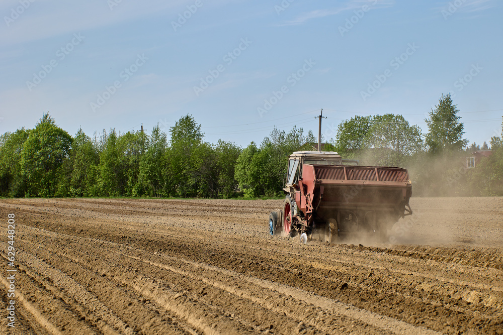 Fototapeta premium Potato planter is hitched to tractor during planting of potatoes during spring sowing period in plowed farmer field.