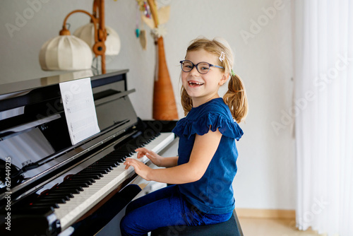 Beautiful little preschool girl playing piano at music school. Cute child having fun with learning to play music instrument. Early musical education for children