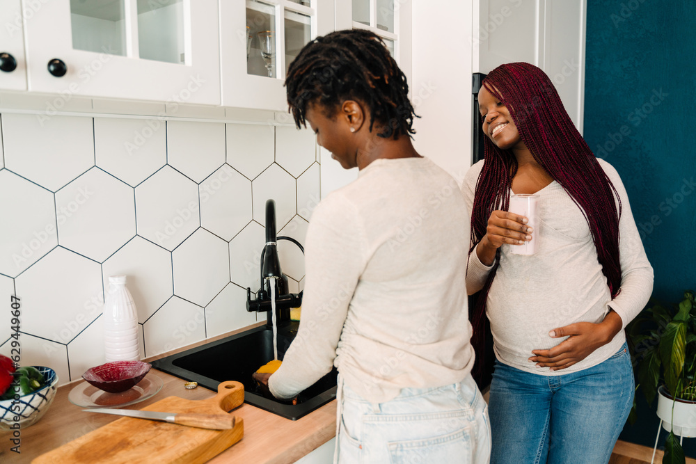 Black lesbian couple smiling while cooking together in kitchen Black lesbian couple smiling while cooking together in kitchen