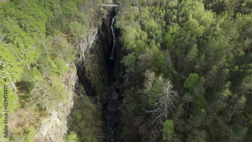 Aerial drone shot flying away from  waterfall inside narrow Corrieshalloch gorge surrounded by forest in Scottish Highlands photo