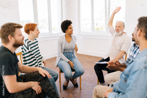 Group of diverse group of people sitting together in circle and raising hands in middle after therapy for high five. Smiling support group celebrating successful session. Friends support mental health © dikushin