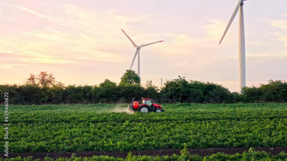 Zoom out span from drone of crop sprayer traktor spraying pesticide or herbicides field. Wind turbines on background. Modern agriculture. Leasing of tractors and agricultural machinery Zoom out span from drone of crop sprayer traktor spraying pesticide or herbicides field. Wind turbines on background. Modern agriculture. Leasing of tractors and agricultural machinery