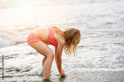 Happy Child  Little Preschool Girl in Swimmsuit Running And Jumping In The Waves During Summer Vacation On Exotic Tropical Beach. Family Journey On Ocean Coast.