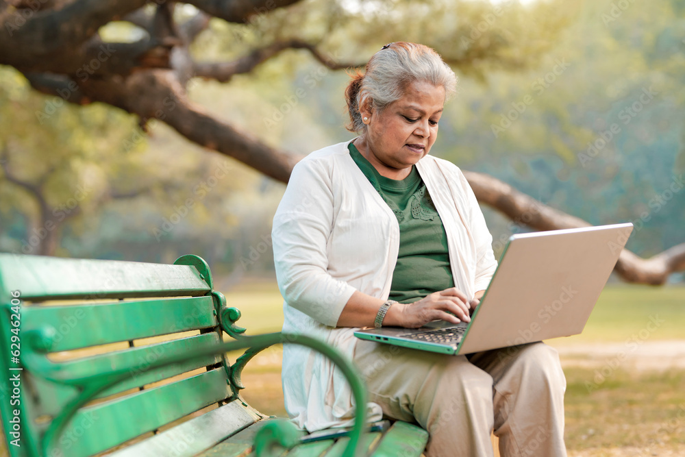 Fototapeta premium Indian senior woman using laptop at park.