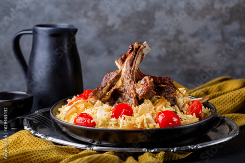 Slow roasted lamb meat on buns with saffron long rice and vegetables, onion, tomatoes, almond. Dinner table with napkin. Haneeth, pilaf, Mansaf, shanks or kabsa. Oriental food, dark background. photo