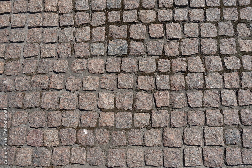Uneven surface of pavement made of rectangular pink granite stone setts