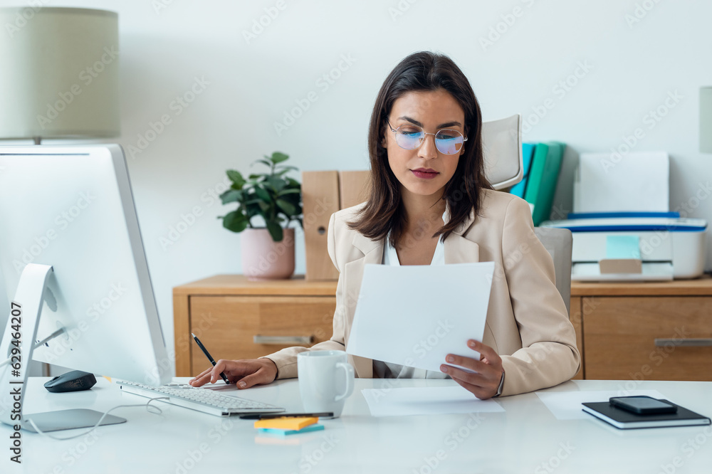 Elegant smart business woman working with computer while reading some notes in the office Elegant smart business woman working with computer while reading some notes in the office