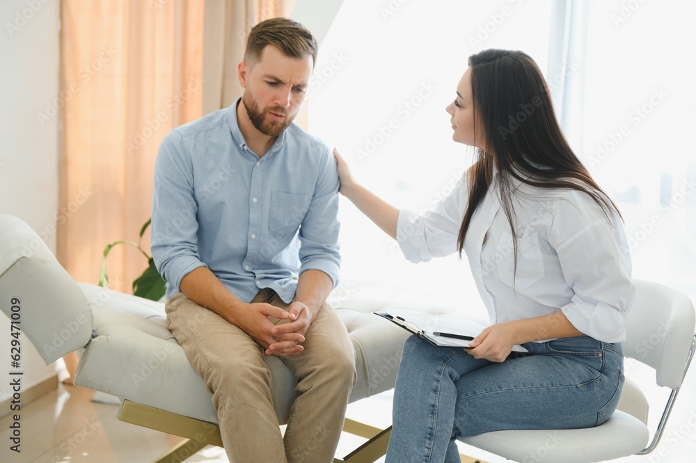 Obraz premium Depressed man speaking to a therapist while she is taking notes
