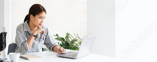 asian woman holding glasses eyewear staring at laptop screen, makes assignment, concentrated, search solution or ideas. Business challenge, thinks over task concept panorama banner copy space