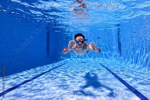 Man with cyberpunk glasses photographed under blue water in a swimming pool