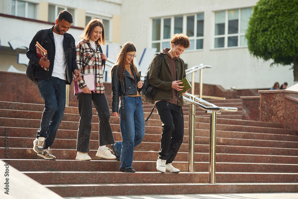 Obraz premium Going down the stairs. Four young students in casual clothes are together outdoors
