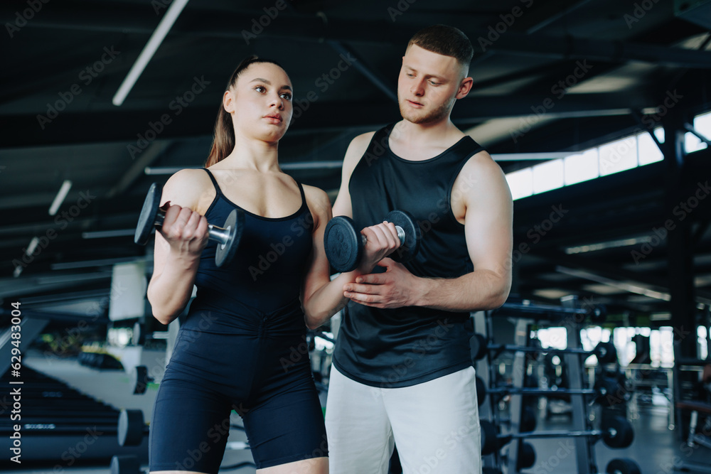 A male personal trainer helps a woman with her dumbbell workout, providing expertise and encouragement in the gym. Fitness Motivation Male Personal Trainer Assisting Woman in Gym A male personal trainer helps a woman with her dumbbell workout, providing expertise and encouragement in the gym. Fitness Motivation Male Personal Trainer Assisting Woman in Gym