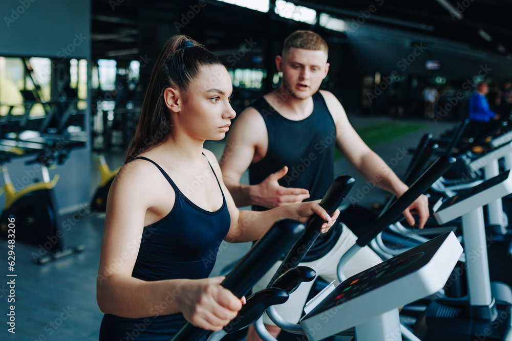 A dedicated fitness trainer instructing a young man and a woman during a dynamic workout session in a well-equipped gym, promoting a healthy and active lifestyle. A dedicated fitness trainer instructing a young man and a woman during a dynamic workout session in a well-equipped gym, promoting a healthy and active lifestyle.