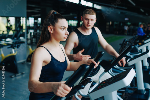A dedicated fitness trainer instructing a young man and a woman during a dynamic workout session in a well-equipped gym, promoting a healthy and active lifestyle.