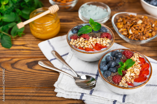 Bowl of granola with yogurt and fresh berries on a texture table. Yogurt berries, acai bowl, spirulina bowl. Healthy food, balanced breakfast. Strawberries, blueberries, kiwi, peach, almonds and chia.