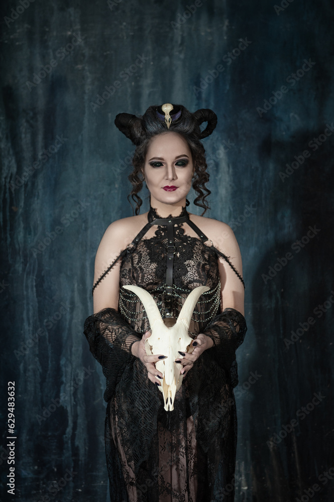 Beautiful woman witch with horns standing in the room and holding goat skull Beautiful woman witch with horns standing in the room and holding goat skull