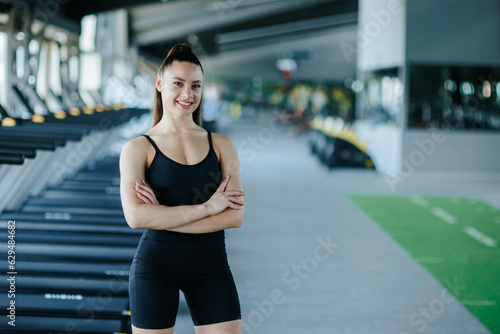 captivating gym portrait, an athletic young woman exudes confidence as she strikes a pose, showcasing her fitness prowess. Her radiant smile and joyful expression reflect her satisfaction