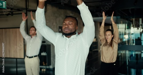 A Black business man in a white shirt is doing yoga with his colleagues in the office. Take a break from work to maintain spiritual strength and stability photo