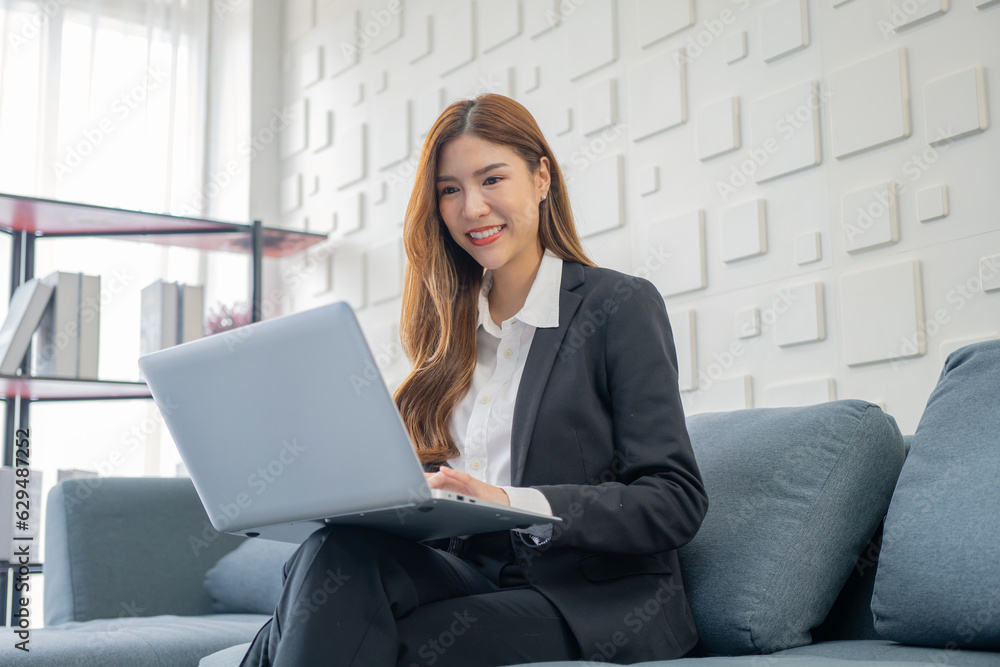 Image of a young beautiful Asian Business woman smiling while working with a laptop and talking to work doing math finance on an office desk, tax, report, accounting, statistics, and research concepts Image of a young beautiful Asian Business woman smiling while working with a laptop and talking to work doing math finance on an office desk, tax, report, accounting, statistics, and research concepts