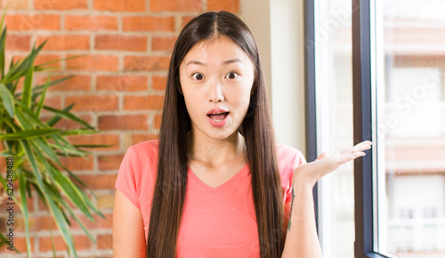 asian pretty woman at home against brick wall with a plant