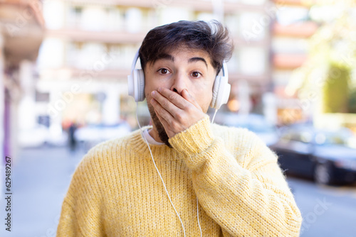 young handsome man covering mouth with a hand and shocked or surprised expression. listening music with headphones photo