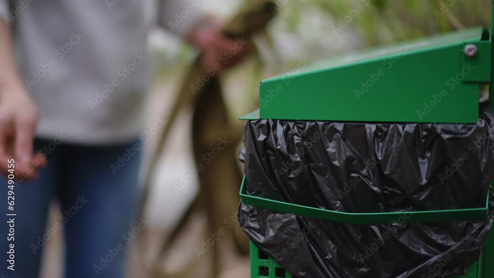 Closeup special trash can in park with unrecognizable woman throwing away dog poop leaving