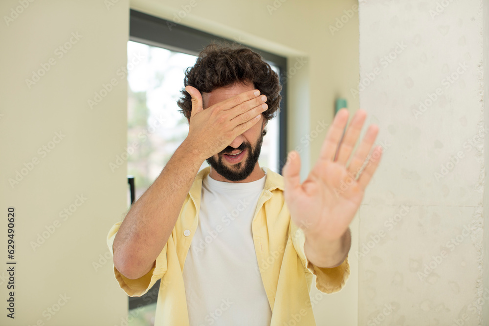 young crazy bearded man covering face with hand and putting other hand up front to stop camera, refusing photos or pictures young crazy bearded man covering face with hand and putting other hand up front to stop camera, refusing photos or pictures