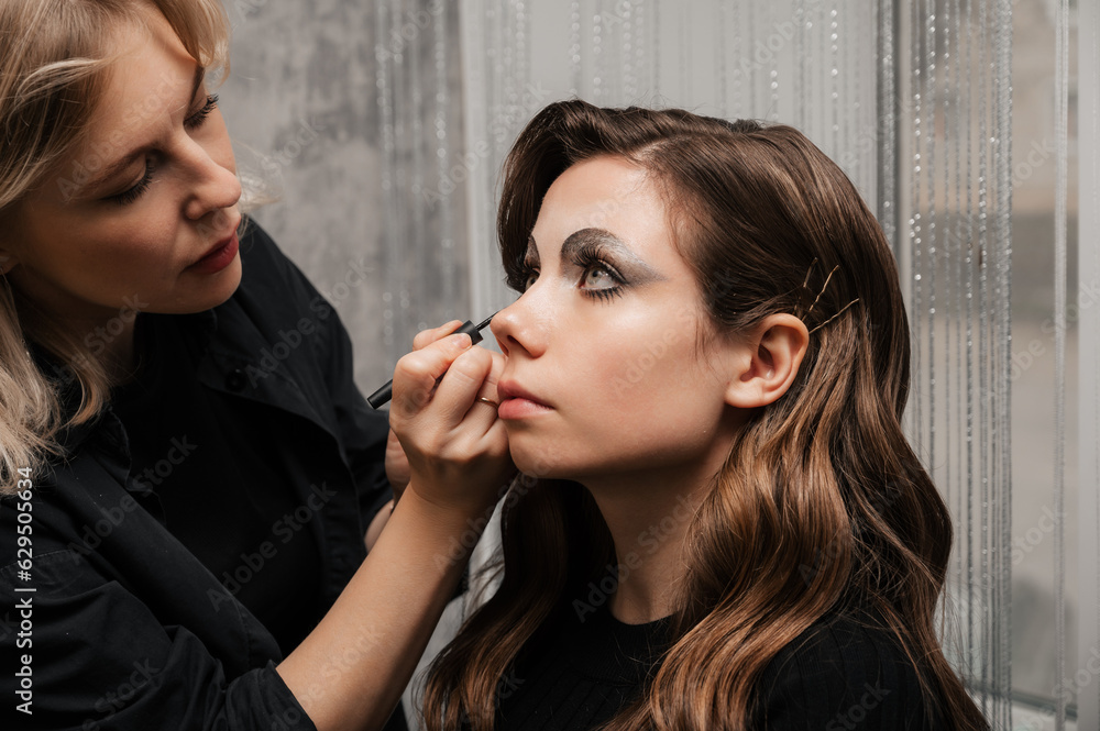 A makeup artist makes eye makeup art for a young girl in a beauty salon. The concept of celebrating Halloween. Unusual makeup. A makeup artist makes eye makeup art for a young girl in a beauty salon. The concept of celebrating Halloween. Unusual makeup.