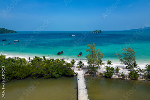 Drone shot of a paradise beach in Koh Rong, Cambodia. Blue water, boats on the water, palm trees on the beach. Paradise climate