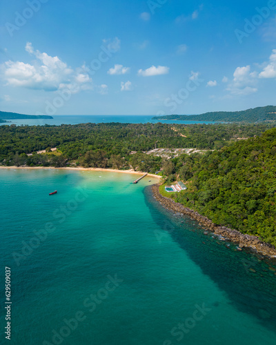 Photo from a drone on the paradise island of Koh Rong Samloem in Cambodia. Blue water, a boat on the water, palm trees on the beach. Paradise atmosphere, villa with a swimming pool.