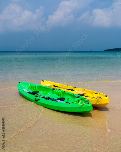Two kayaks on the beach. turquoise water. One green kayak, the other yellow kayak. Paddles in kayaks. Cambodia
