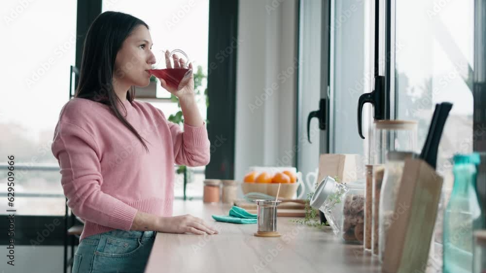 Video of beautiful young woman drinking tea while standing in the kitchen at morning Video of beautiful young woman drinking tea while standing in the kitchen at morning