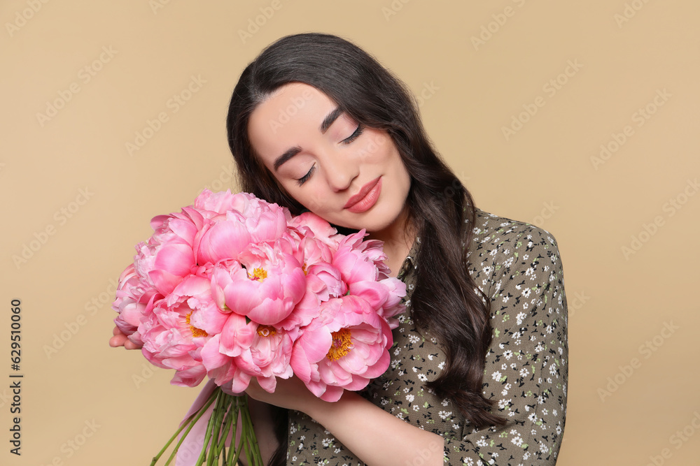 Fototapeta premium Beautiful young woman with bouquet of pink peonies on light brown background