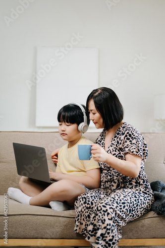 Homeschool Asian young little boy learning online and does homework by using computer and tablet with mother help, teach and encourage. son smile to study at home together