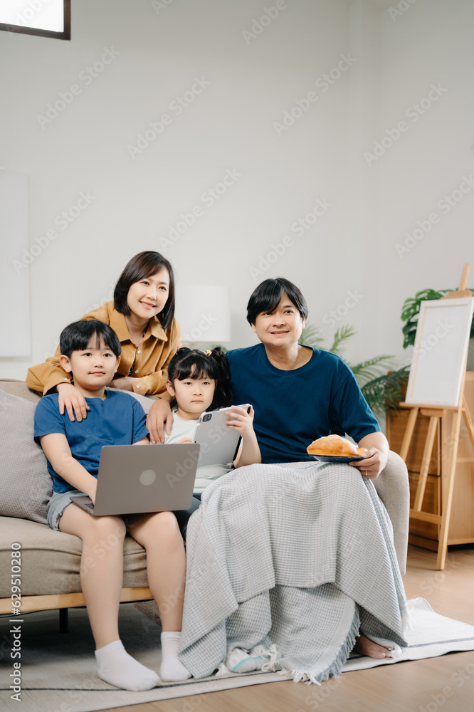Asian parents and kids laugh use devices together sit on sofa, tech addicted family with children hold laptop phone digital tablet having fun at home Asian parents and kids laugh use devices together sit on sofa, tech addicted family with children hold laptop phone digital tablet having fun at home