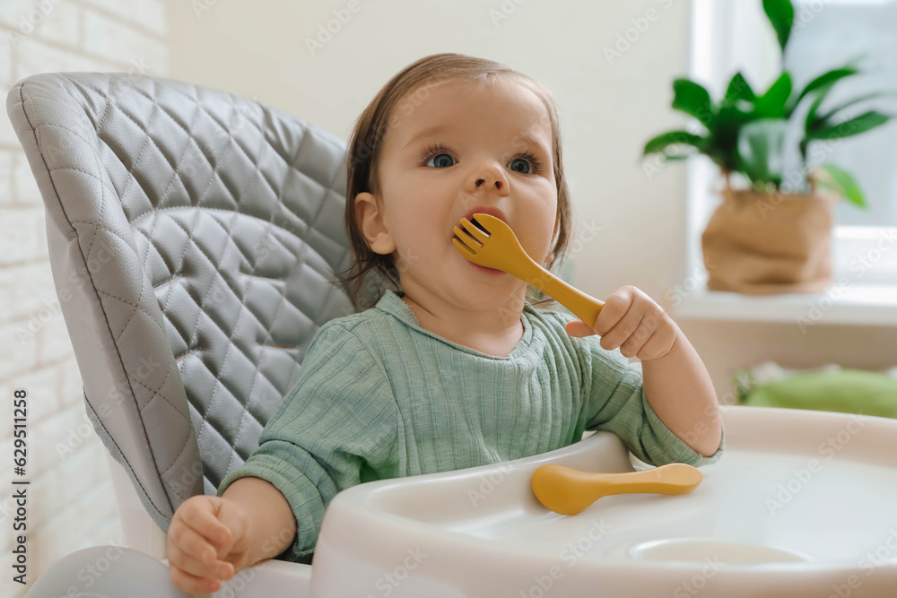 Cute little baby nibbling fork in high chair indoors Cute little baby nibbling fork in high chair indoors