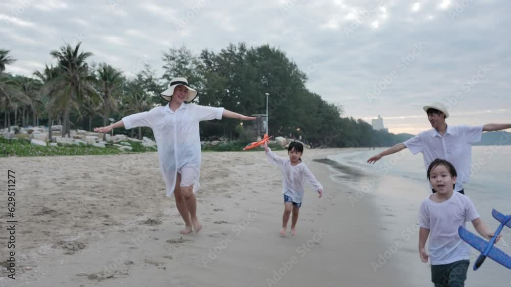 Happy Asian family of father, mother, son, and daughter playfully run and pretend to fly like planes on the beach. Capturing the joy of holiday and travel in slow motion. Happy Asian family of father, mother, son, and daughter playfully run and pretend to fly like planes on the beach. Capturing the joy of holiday and travel in slow motion.