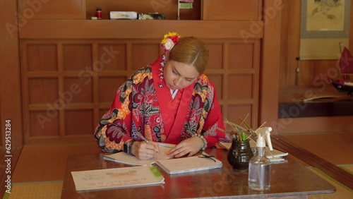 Young latin woman practicing japanese writing at Okinawa world wearing kimono Ryusou dress in traditional japan wood house durgin summer photo