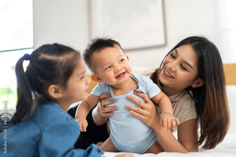 Portrait of enjoy happy love family asian mother playing with adorable little asian baby and sister girl, newborn, infant.Mom touching care with cute son in a white bedroom.Love of family concept Portrait of enjoy happy love family asian mother playing with adorable little asian baby and sister girl, newborn, infant.Mom touching care with cute son in a white bedroom.Love of family concept