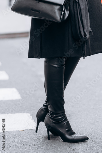 Young stylish woman walking in autumn city, cold season, wearing high heeled leather black high boots. Street style outfit