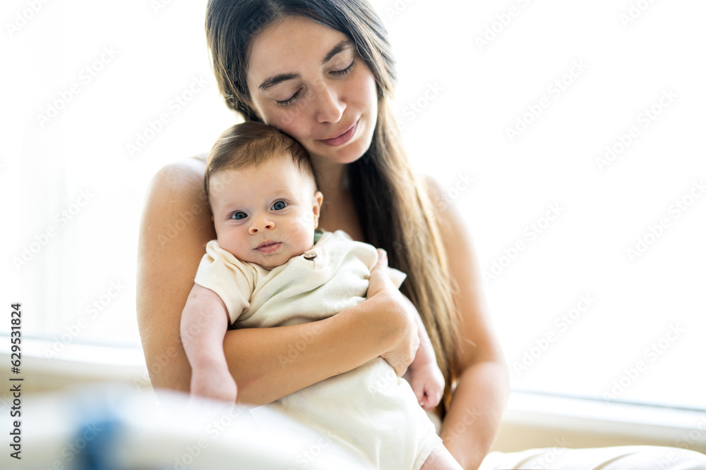 Young mother holding her newborn baby boy at home in living room. Young mother holding her newborn baby boy at home in living room.