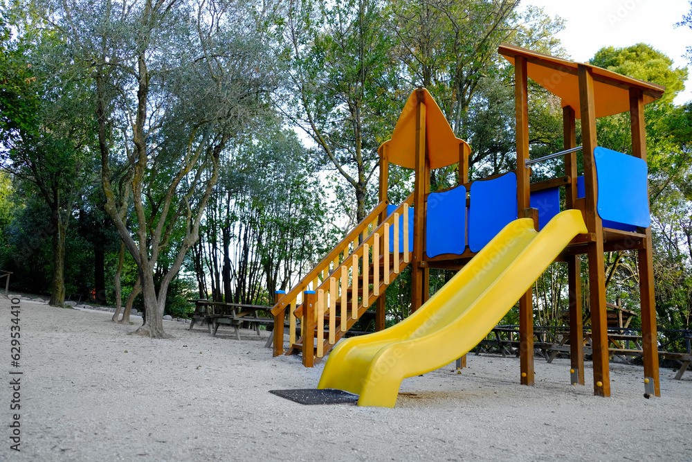 Empty playground with beautiful slide, benches and trees in park. Space for text