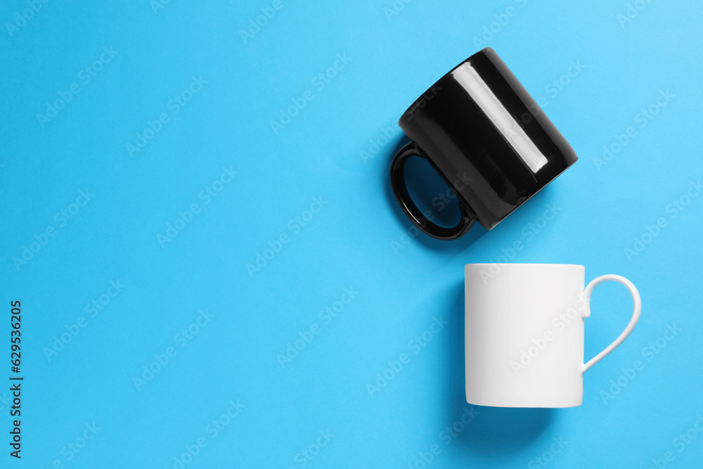 White and black ceramic mugs on light blue background, flat lay. Space for text White and black ceramic mugs on light blue background, flat lay. Space for text