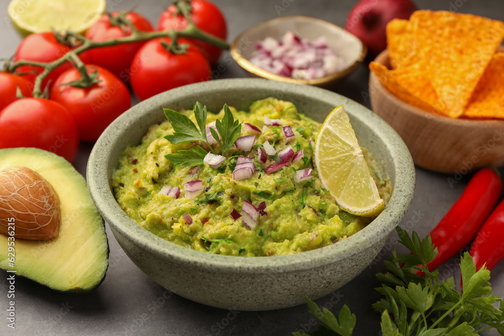 Bowl of delicious guacamole, nachos chips and ingredients on grey table, closeup Bowl of delicious guacamole, nachos chips and ingredients on grey table, closeup