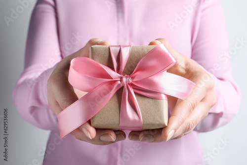 Fototapeta Naklejka Na Ścianę i Meble -  Woman holding gift box with pink bow on light grey background, closeup
