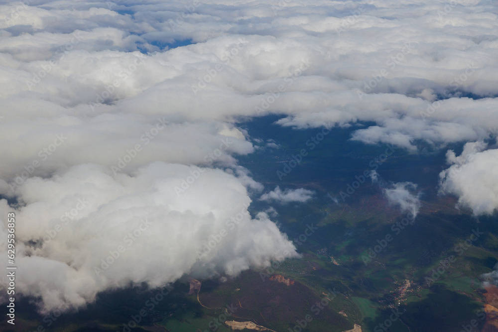 Obraz premium An airplane window offers wonderful view of beautiful landscape of green mountains with fluffy blue clouds in background