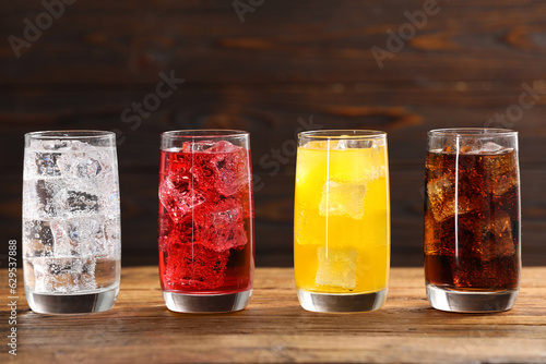 Glasses of different refreshing soda water with ice cubes on wooden table